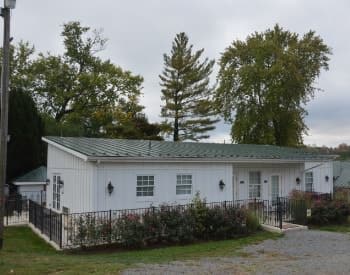 Exterior view of Chicken Coop painted white with green roof surrounded by rod iron fence and rose bushes