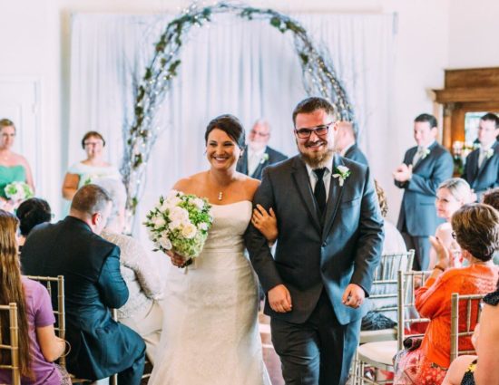 Bride in white dress and groom in gray suit walking down the aisle together