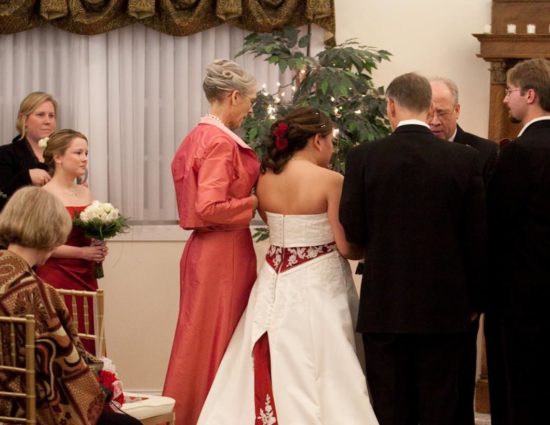 Bride in white dress with red accents and groom in black suit standing at the alter