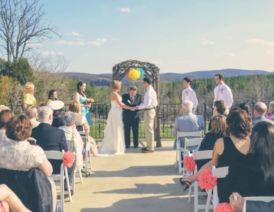 Patio set up for wedding ceremony with bridal party in teal dresses, bride in white dress, and groom and groomsmen in white shirts and khaki pants