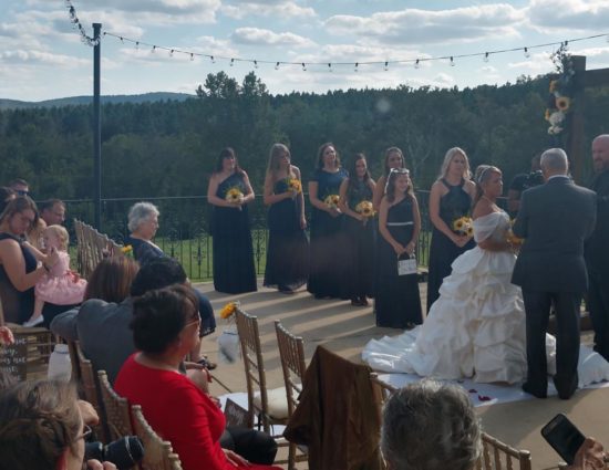 Patio set up for wedding ceremony with bridal party in navy dresses, bride in white, and groomsmen in gray suits