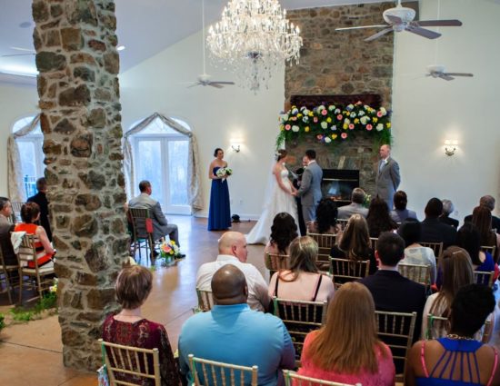 Large room with concrete flooring set up for a wedding ceremony with the maid of honor in a blue dress and best man in a gray suit