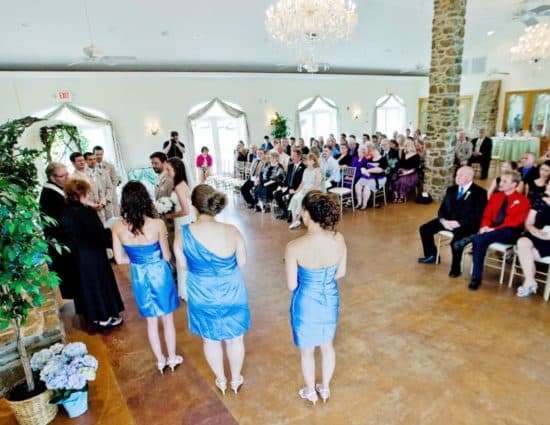 Large room with concrete flooring set up for a wedding ceremony with the wedding party in blue dresses and light tan suits