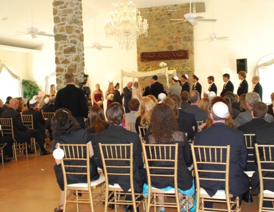 Large room with concrete flooring set up for a wedding ceremony with the wedding party in burgundy dresses and black suits