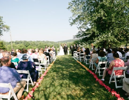 Wedding ceremony near large tree with green leaves with bride in white dress and groom in black suit