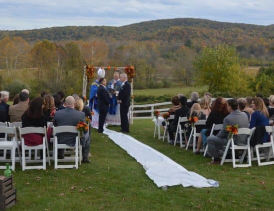 Wedding ceremony with rolling hills in the background and two grooms with dark blue suits