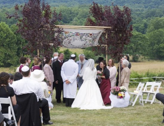 Wedding ceremony with rolling hills of green trees in the background with bride in white dress and groom in white robe