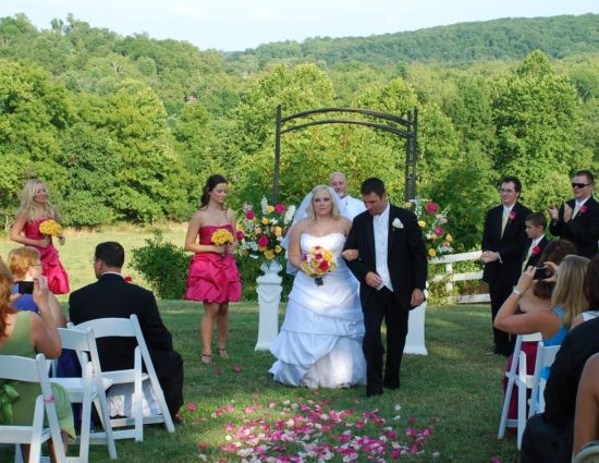 Wedding ceremony with rolling hills filled with green trees in the background with bride in white dress and groom in black suit