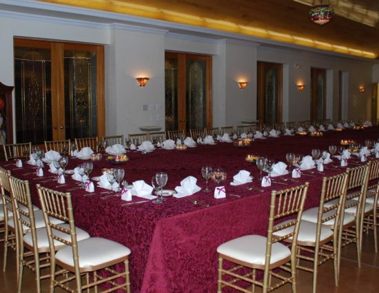 Large room with concrete flooring set up for wedding reception with burgundy tablecloths and white napkins