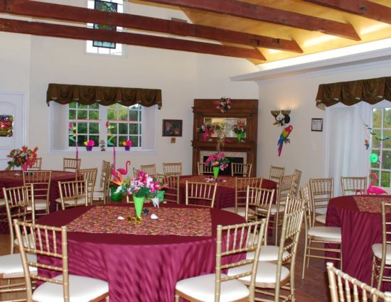 Large room with hardwood flooring set up for wedding reception with burgundy tablecloths