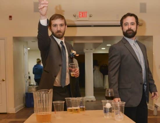 Two men with gray suits playing beer pong