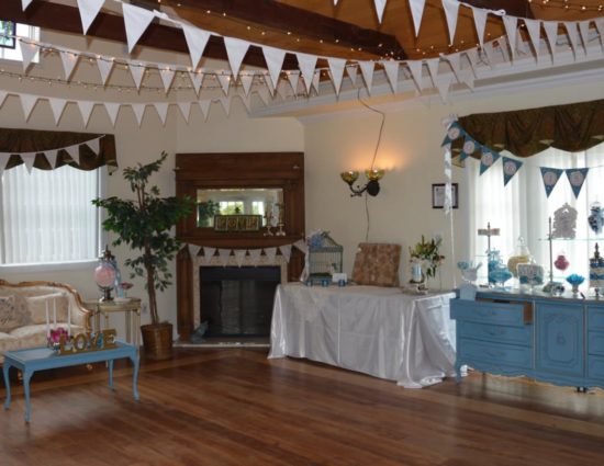 Large room with hardwood flooring, upholstered couch, coffee table, fireplace in the corner, long table with white tablecloth, and old vintage blue buffet table