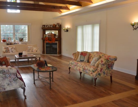 Large room with hardwood flooring, dark wood China hutch, upholstered couches, coffee tables, and fireplace in the corner