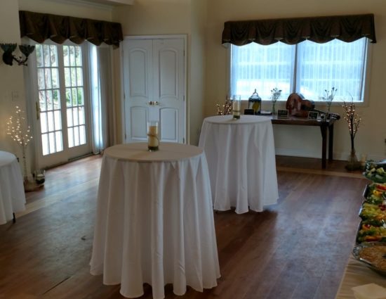 Large room set up with cocktail and round tables with white tablecloths and a table with appetizers