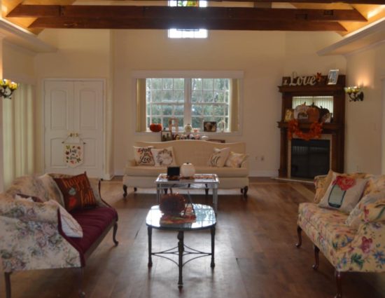 Large room with hardwood flooring, dark wood China hutch, upholstered couches, coffee tables, and fireplace in the corner