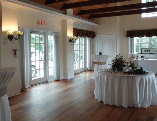 Large room with hardwood flooring set up for a cocktail reception with tables with white tablecloths