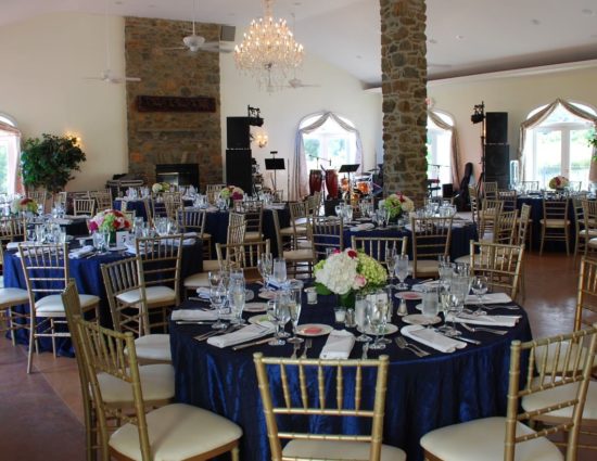 Large room set up for a wedding reception with navy tablecloths and white napkins