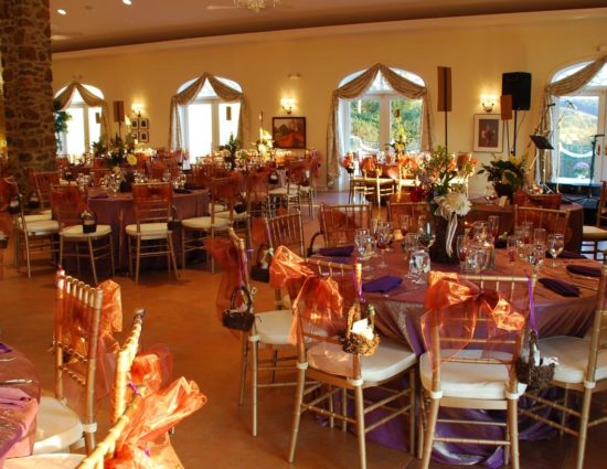 Large room set up for a wedding reception with pink sheer tablecloths and purple napkins