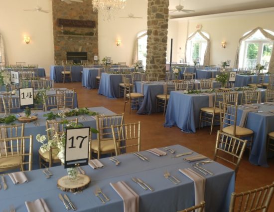 Large room set up for a wedding reception with powder blue tablecloths and gray napkins