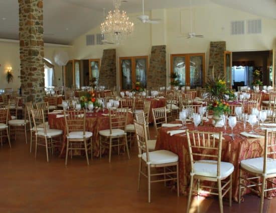 Large room set up for a wedding reception with gold and pink tablecloths and white napkins