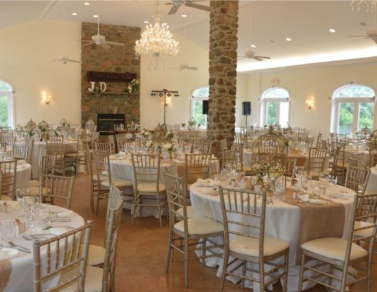 Large room set up for a wedding reception with white and burlap tablecloths