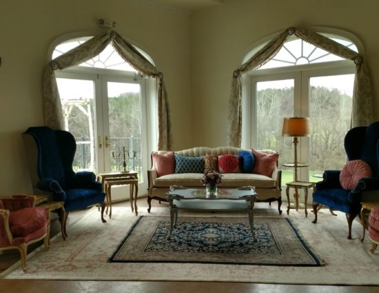 Large room with large area rug, blue and pink upholstered chairs, cream upholstered sofa, coffee table, and end tables