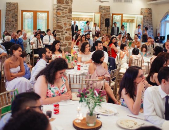 Large room set up for wedding reception with white tablecloths and napkins and people watching the couple