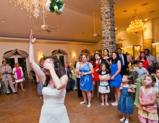 Bride in white dress throwing bouquet to group of ladies