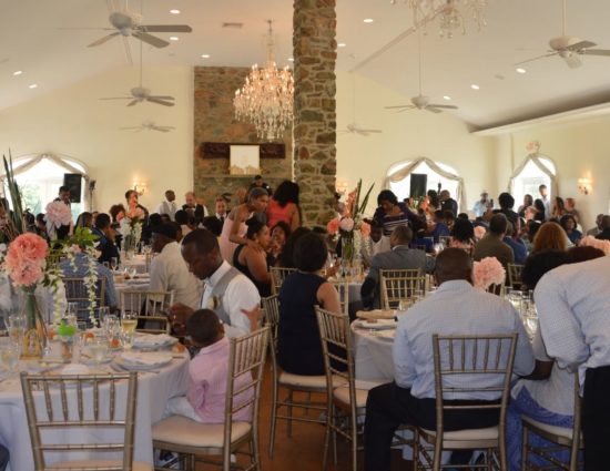 Large room set up for a wedding reception with white tablecloths and napkins and people eating and talking