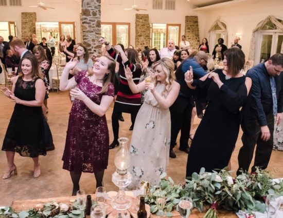 Group of wedding guests doing a line dance in a large room with concrete flooring