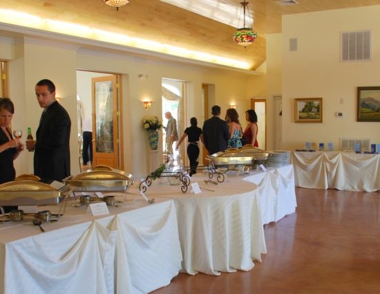 Large room with concrete flooring set up for a wedding reception with white tablecloths and buffet station