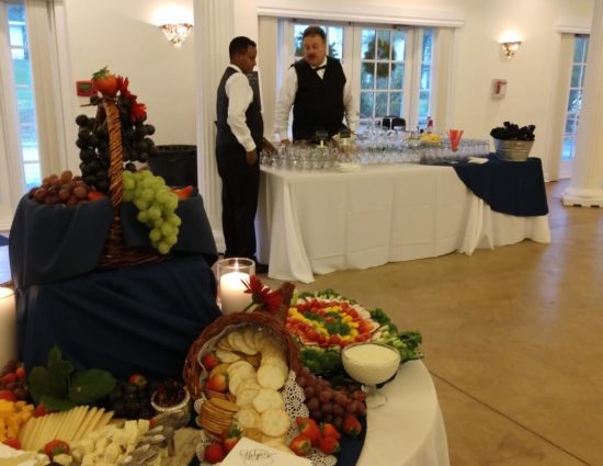 Large room with concrete flooring, large tables with white tablecloths, cheese and crackers station, drink table, buffet table