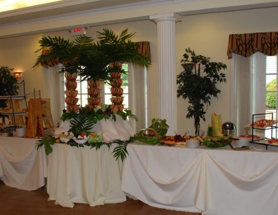 Large room with concrete flooring set up for a wedding reception with white tablecloths and buffet station with lots of food