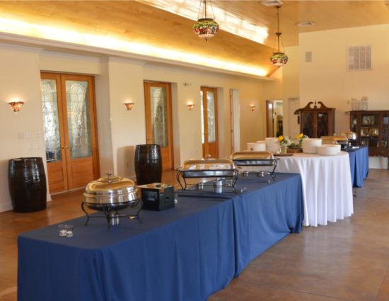 Large room with concrete flooring set up for a buffet with blue and white tablecloths