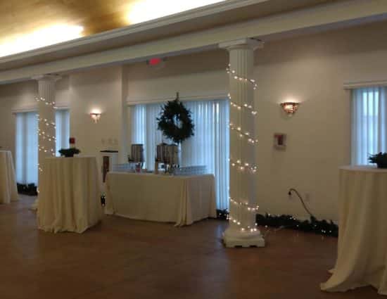 Large room with concrete flooring set up for cocktail reception with tables with white tablecloths and drink station