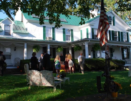 Fall wedding reception set up on green lawn in front of main house painted white with green roof and shutters