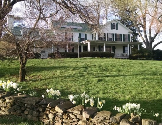 Exterior view of the main house painted white with green roof and shutters with large green lawn and white flowers