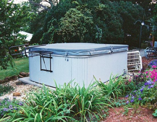 Large hot tub surrounded by green trees, green grasses, and purple and pink flowers