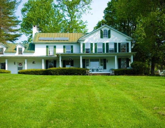 Exterior view of the main house painted white with green roof and shutters surrounded by green trees and large green lawn