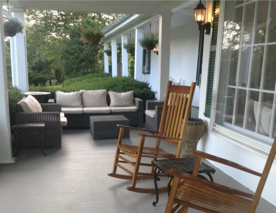 Front porch with dark gray wicker patio furniture with tan cushions and two wooden rocking chairs