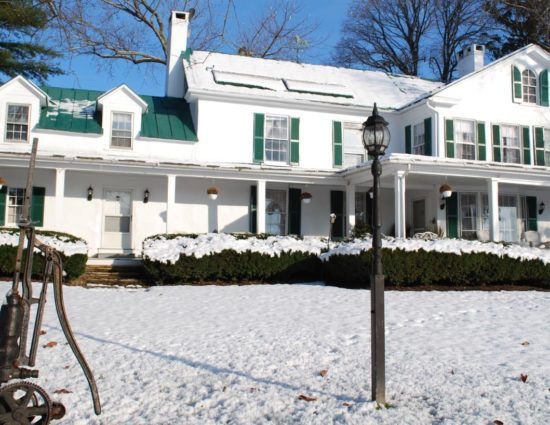 Exterior view of property painted white with green roof and shutters all covered in snow