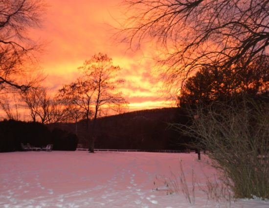 View of large open space covered with snow with the sun rising in the background