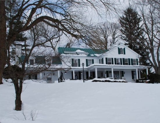 Exterior view of property painted white with green shutters and roof all covered in snow