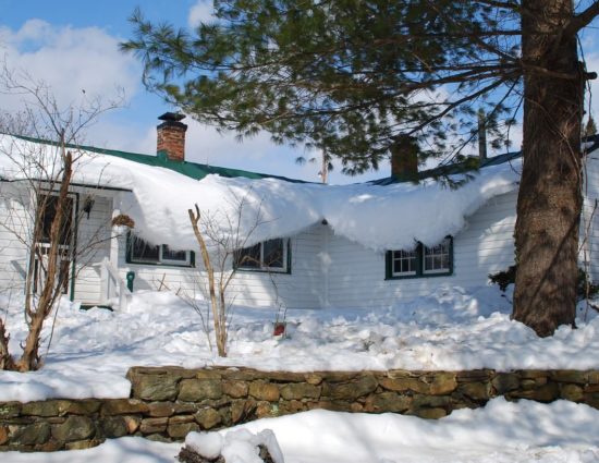 Cottage painted white with green roof covered with snow