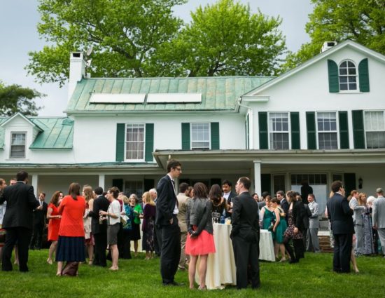 Wedding cocktail reception set up on front lawn of main house painted white with green shutters