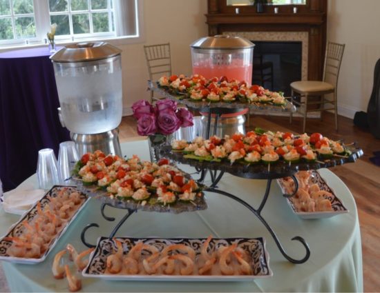 Round table with light green tablecloth filled with serving platters with appetizers and water and punch dispensers