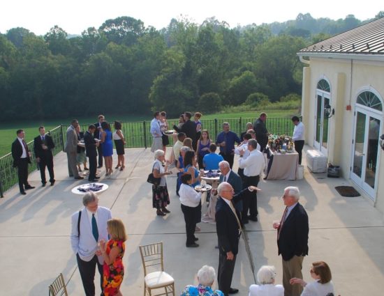 Large concrete patio set up for wedding cocktail reception with people standing around talking