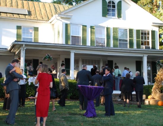 Wedding cocktail reception set up on front lawn of main house painted white with green shutters