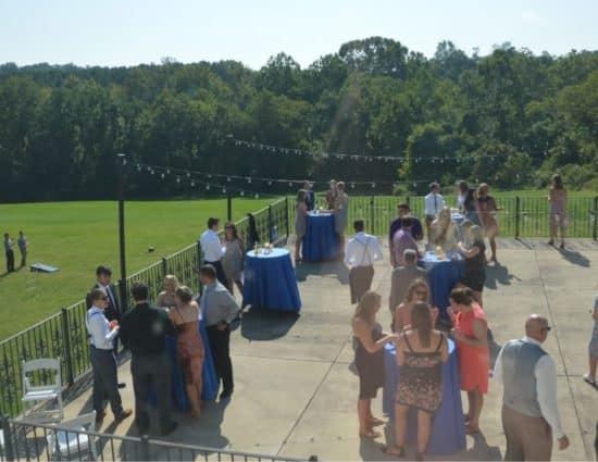 Large concrete patio set up for wedding cocktail reception overlooking large green lawn and green trees