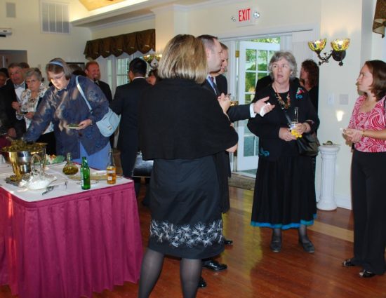 Large room with hardwood flooring set up for wedding reception with people standing around talking and getting food